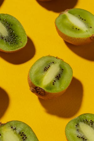 Halved kiwi fruit arranged on a yellow background, showcasing their green flesh and black seeds.