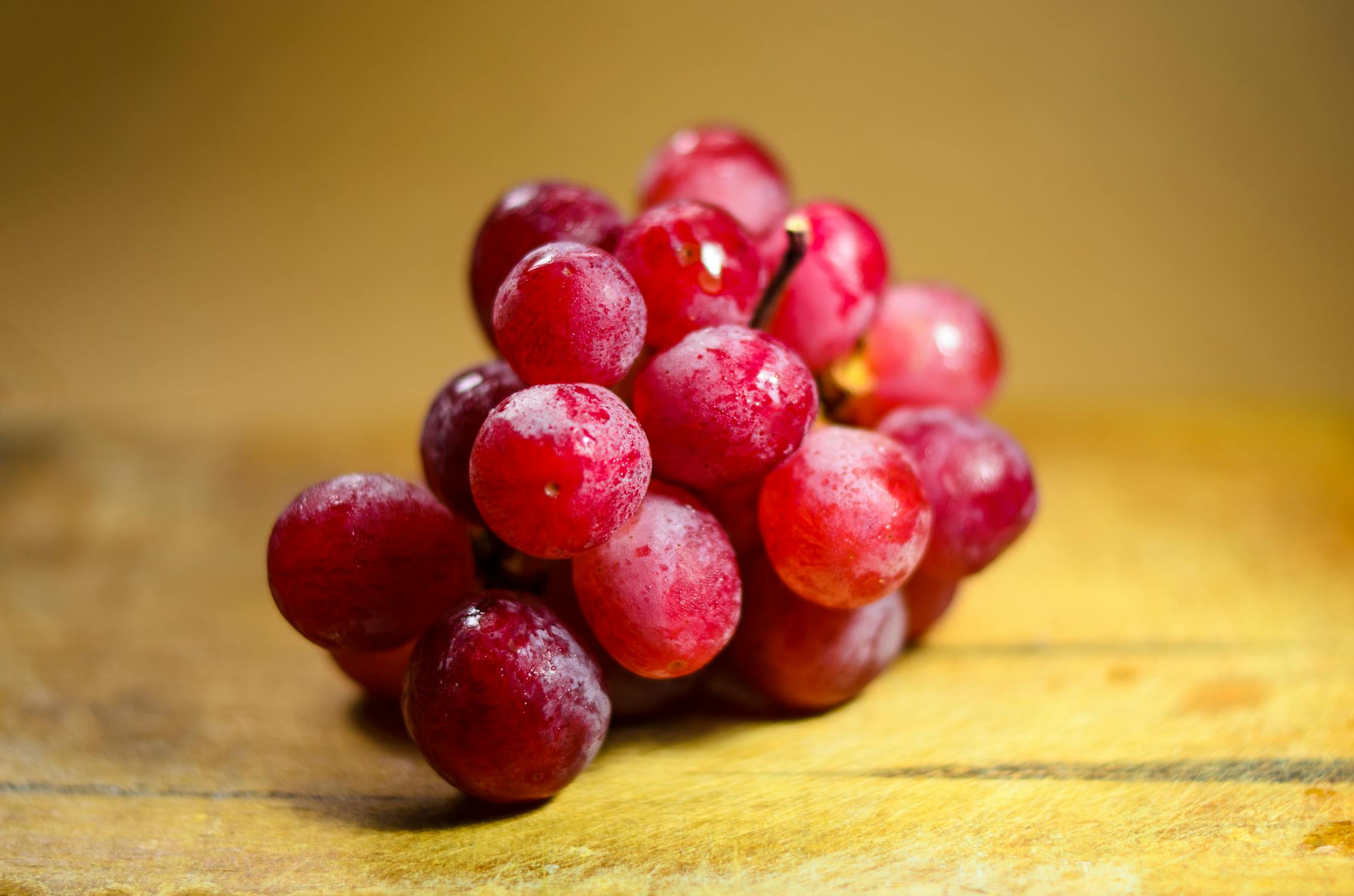 A close-up of a bunch of red grape fruits on a wooden surface.