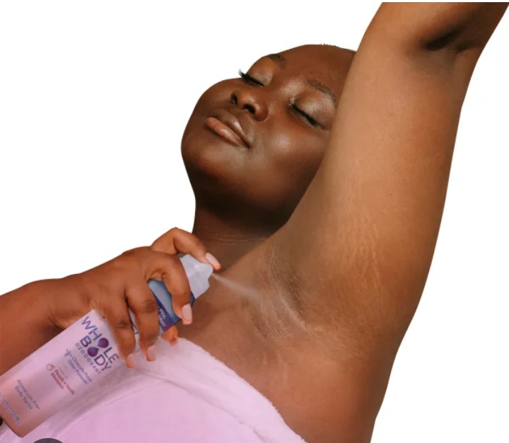 A black skinned lady applying a spray deodorant 